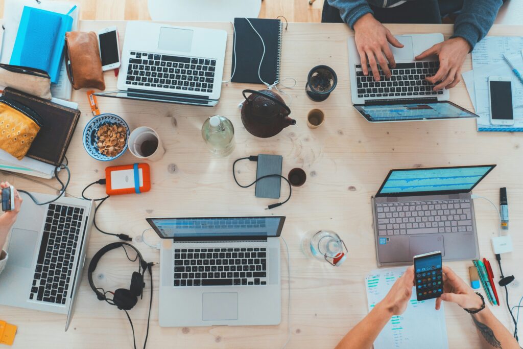 Schreibtisch von oben mit 6 Laptops und Getränken